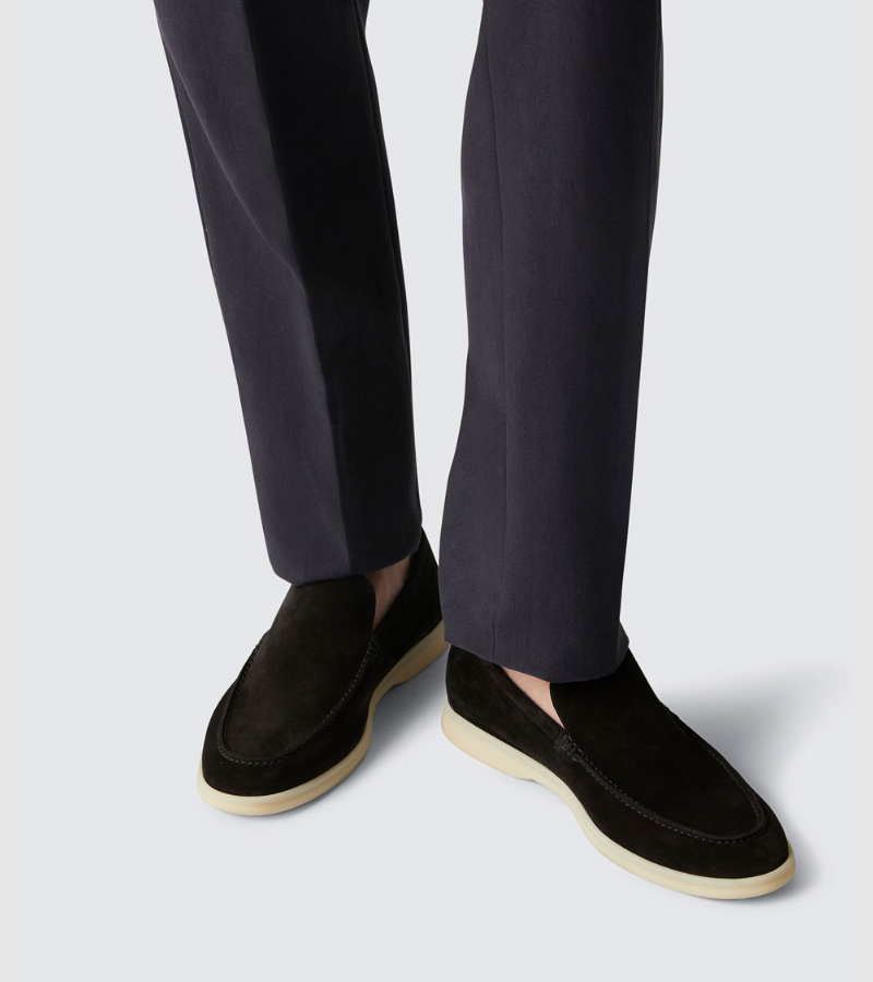 Black loafers worn with dark trousers on a light background
