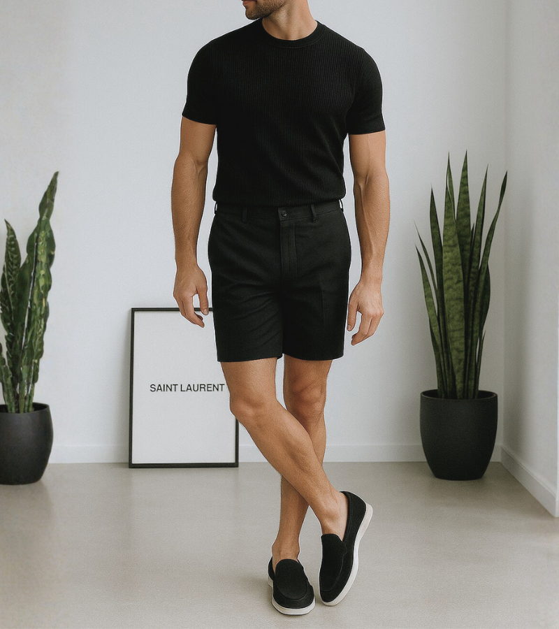 Person wearing a black t-shirt and shorts standing in a minimalistic room with plants and a framed picture.