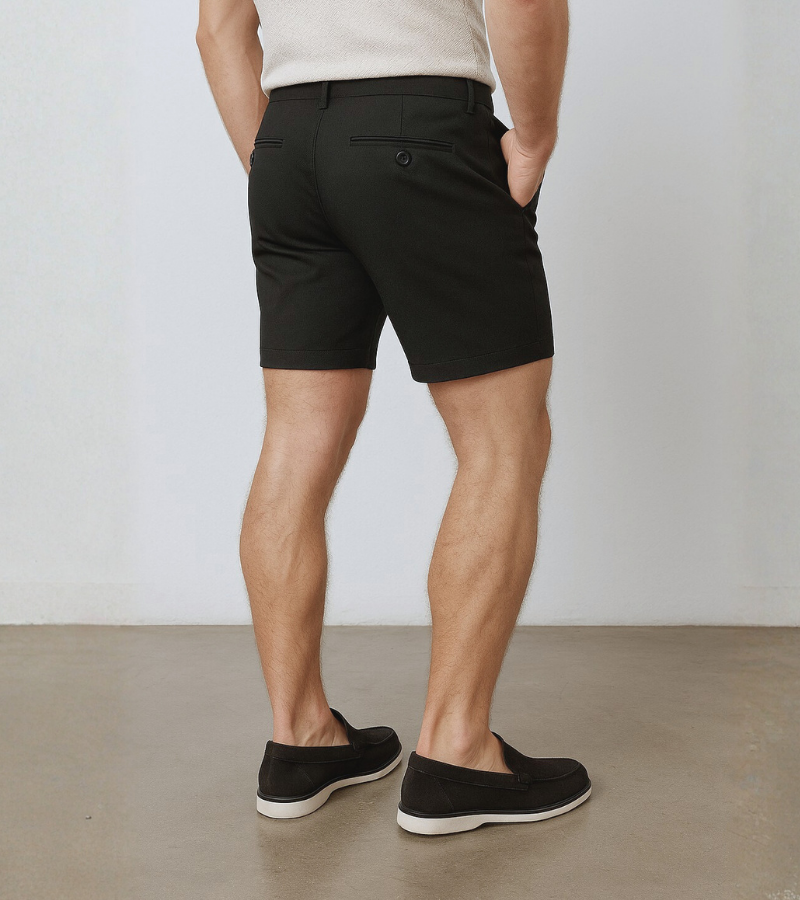 Person wearing black shorts and black shoes on a plain background