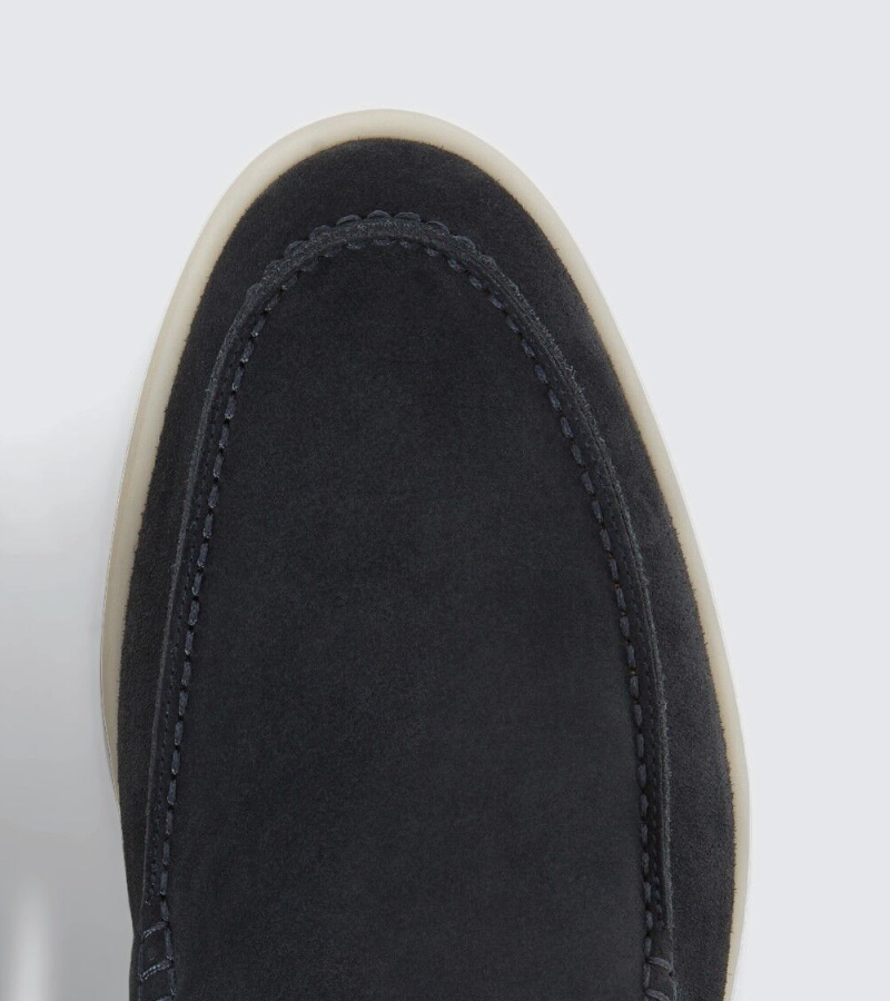 Close-up of a black suede shoe with white sole on a light gray background